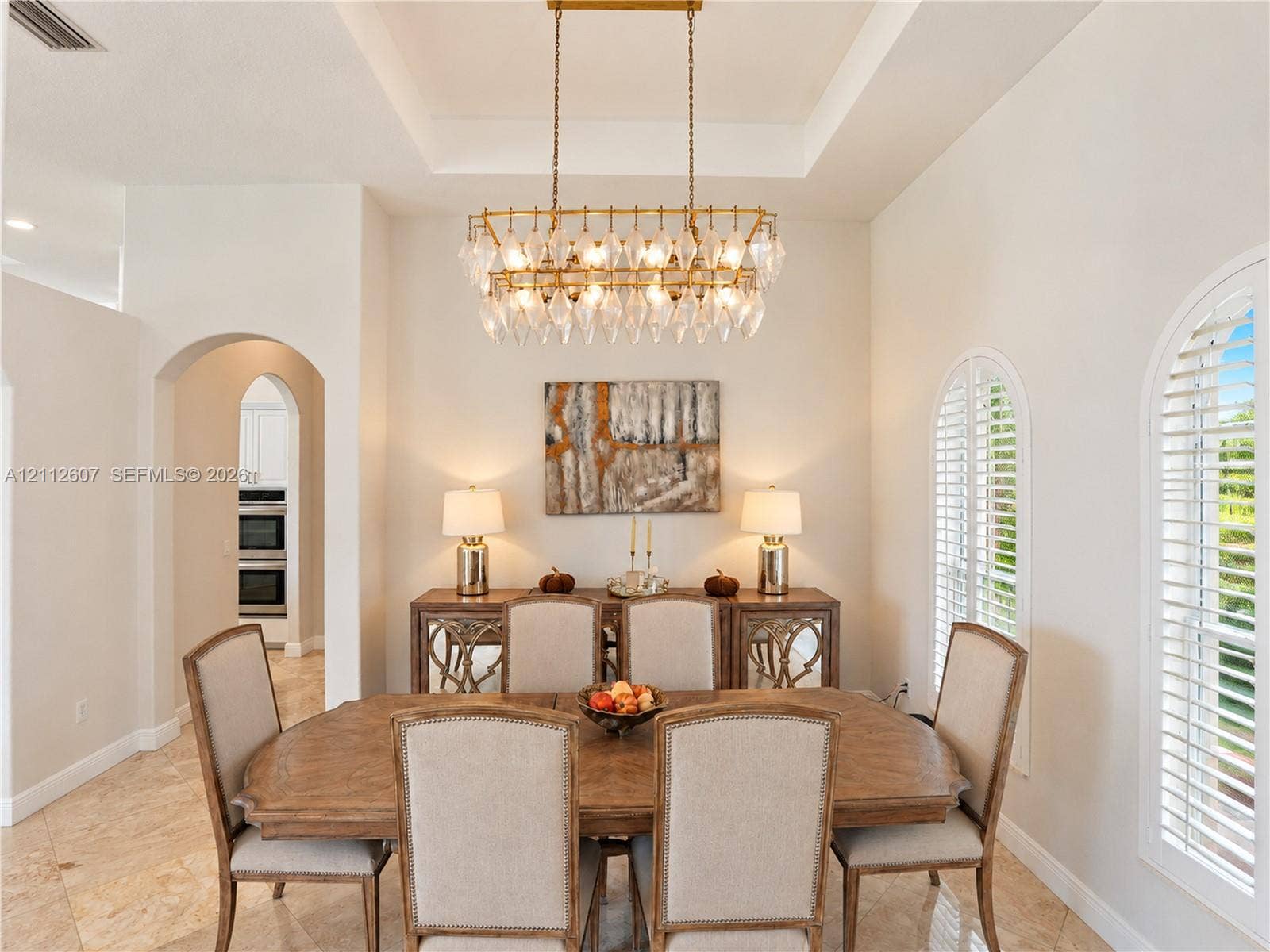 14443 S Jockey Circle S, Davie, FL 33330 Tray ceiling with recessed lighting, tiered crystal chandelier, tile flooring, and arched windows featuring plantation shutters