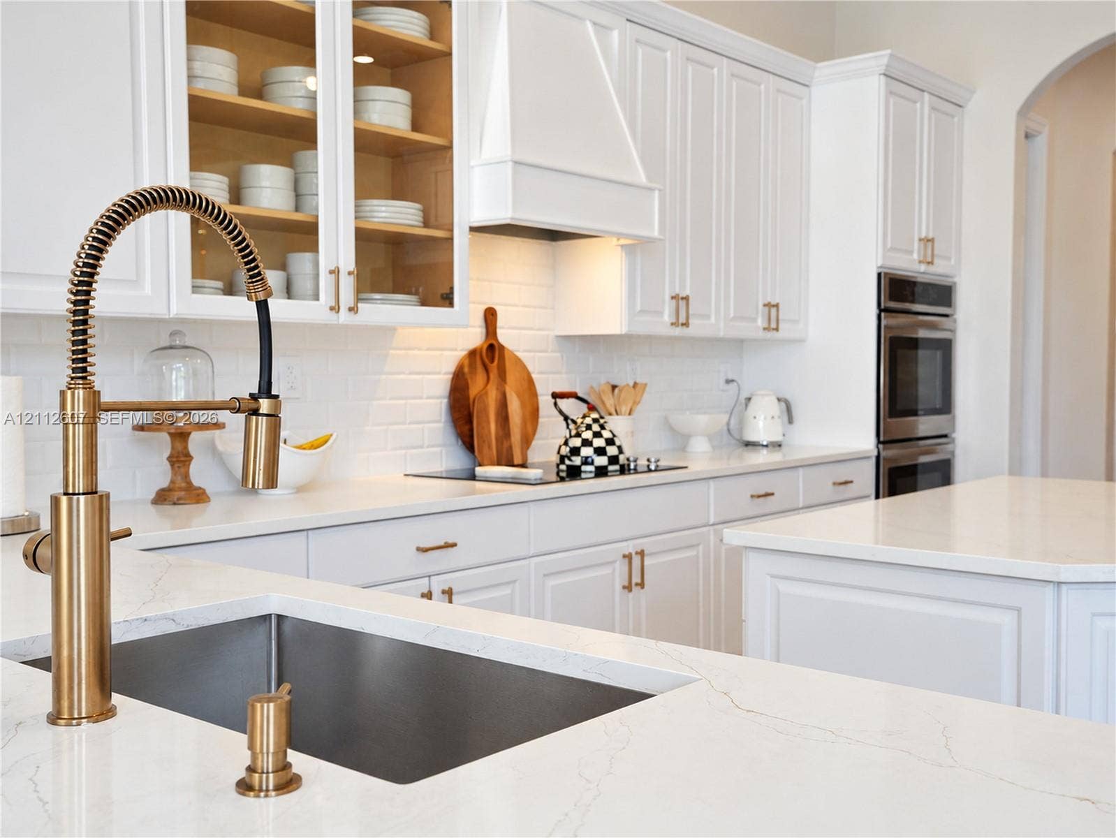 14443 S Jockey Circle S, Davie, FL 33330 Kitchen featuring white cabinetry with gold-tone hardware, stone countertops, a subway tile backsplash, a high-arc professional style faucet, and built-in double wall ovens
