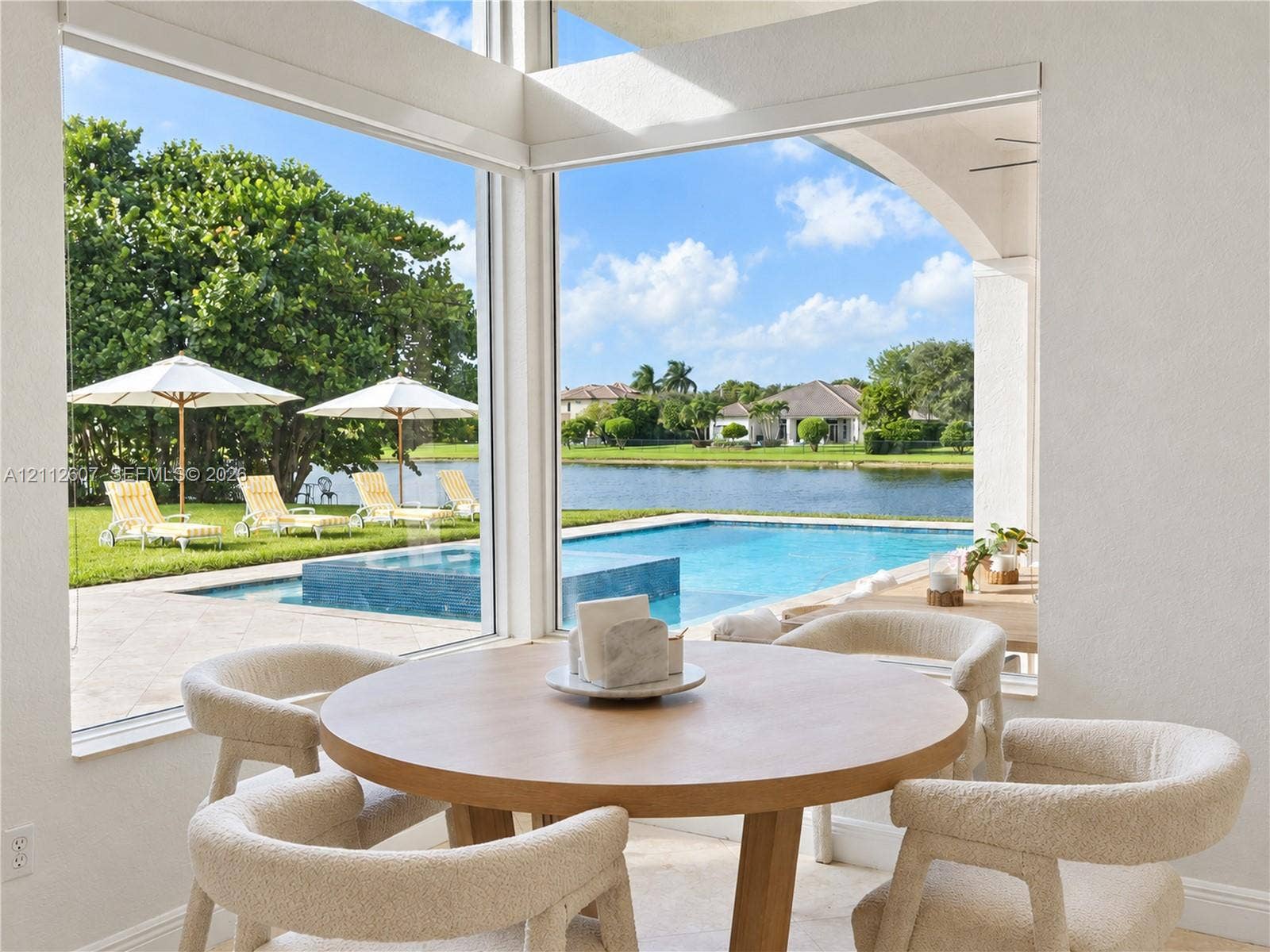 14443 S Jockey Circle S, Davie, FL 33330 Floor-to-ceiling corner windows showcasing a paved pool deck, a swimming pool with integrated spa, and water frontage