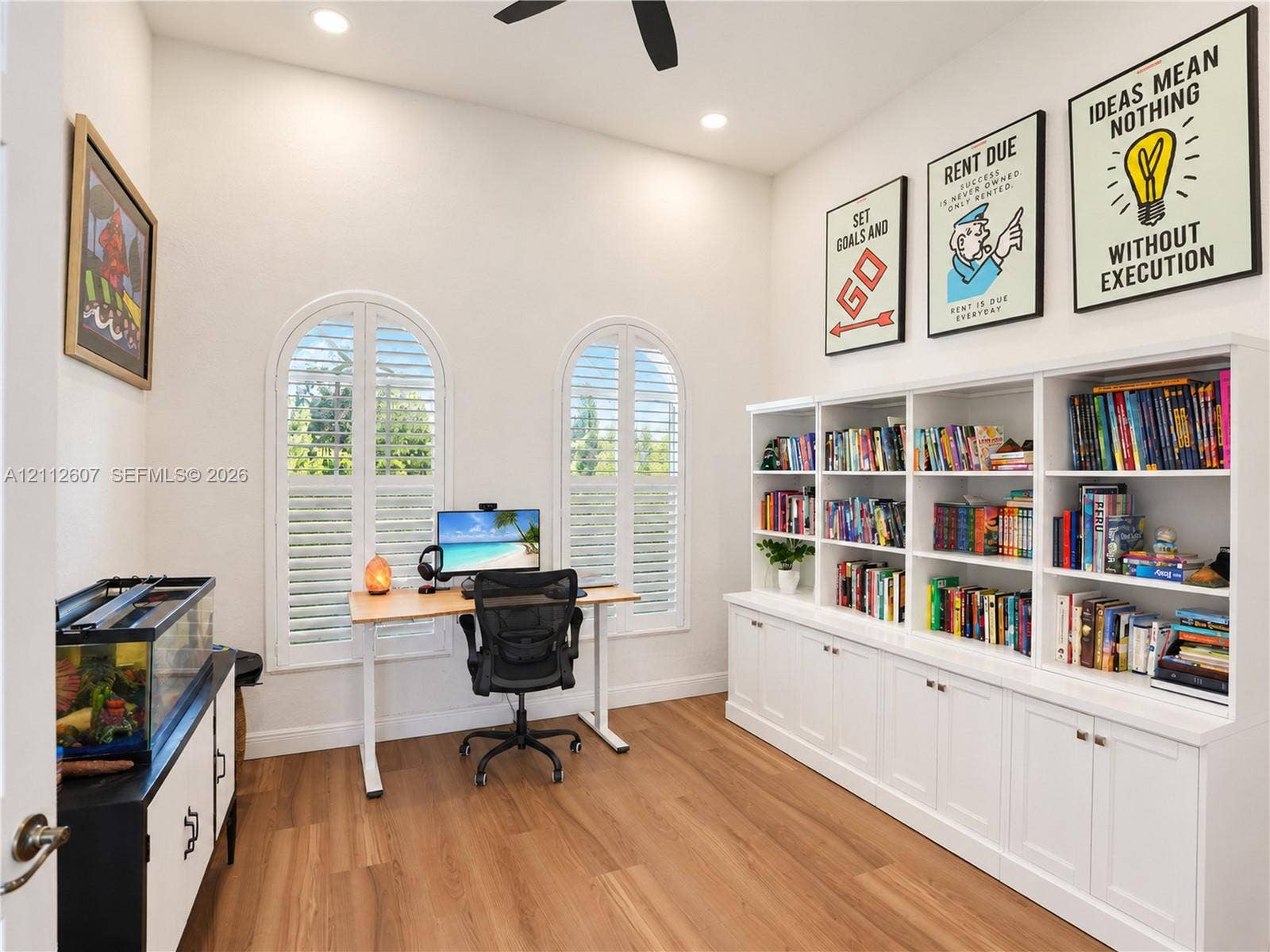 14443 S Jockey Circle S, Davie, FL 33330 High-ceilinged room featuring wood-finish flooring, custom floor-to-ceiling built-in cabinetry, two arched windows with plantation shutters, and a ceiling fan