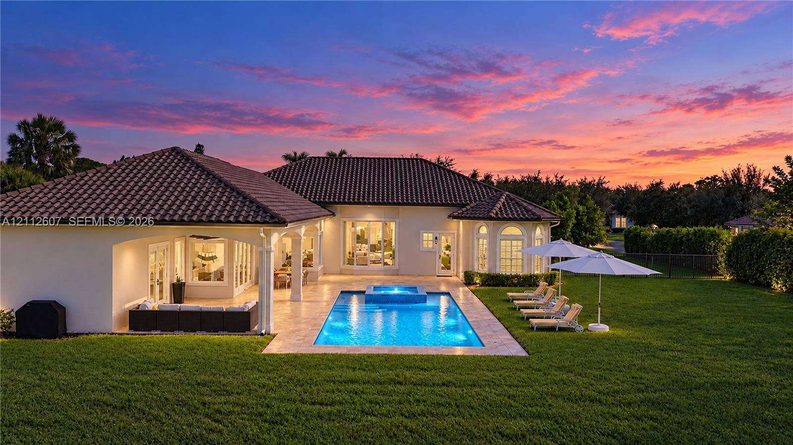 14443 S Jockey Circle S, Davie, FL 33330 Rear exterior featuring a tile roof, stucco facade, stone-paved patio, custom swimming pool with integrated spa, and expansive lawn