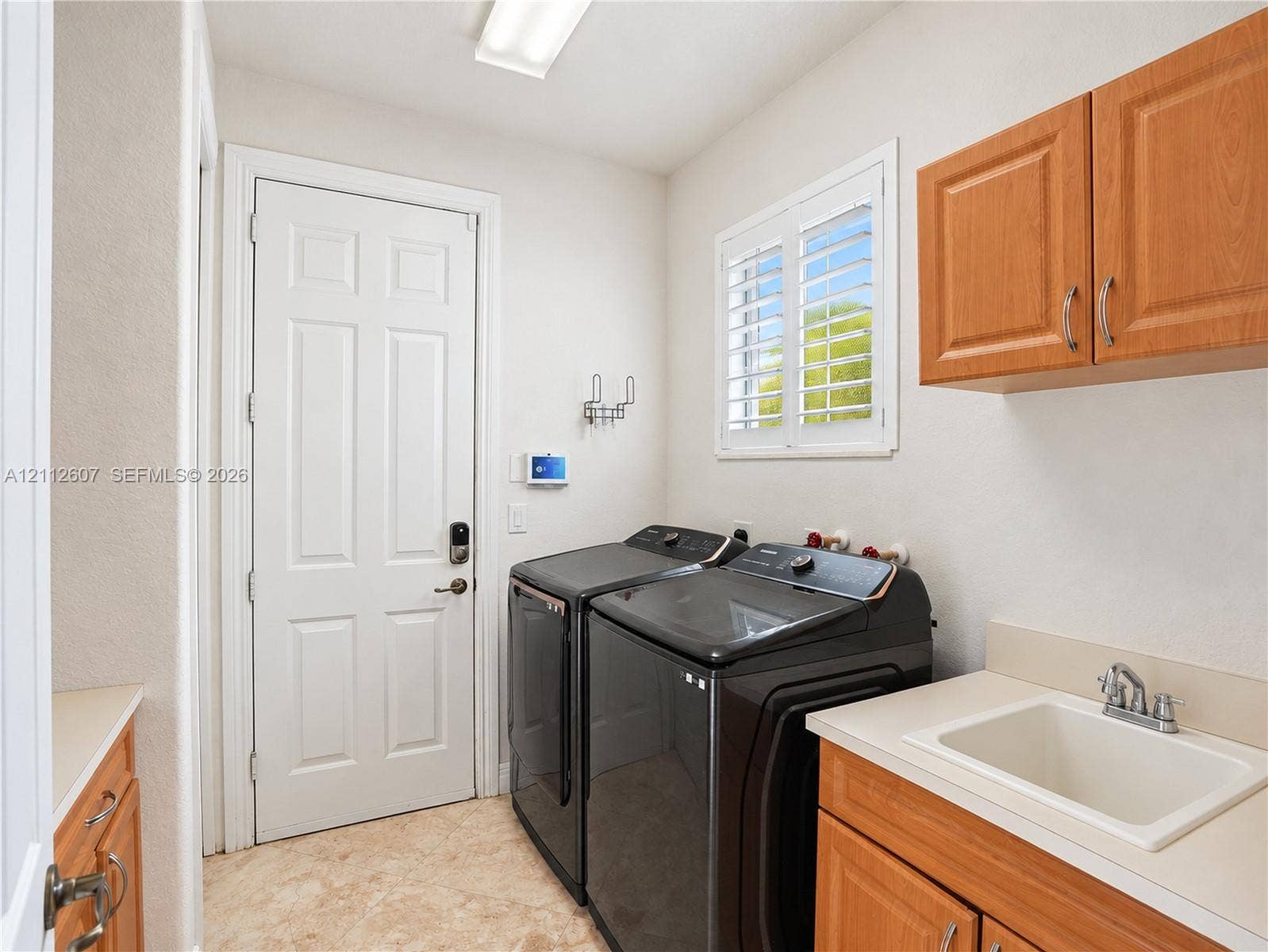 14443 S Jockey Circle S, Davie, FL 33330 Utility room featuring wood-finish cabinetry, a drop-in sink, stone-surface counters, and white plantation shutters