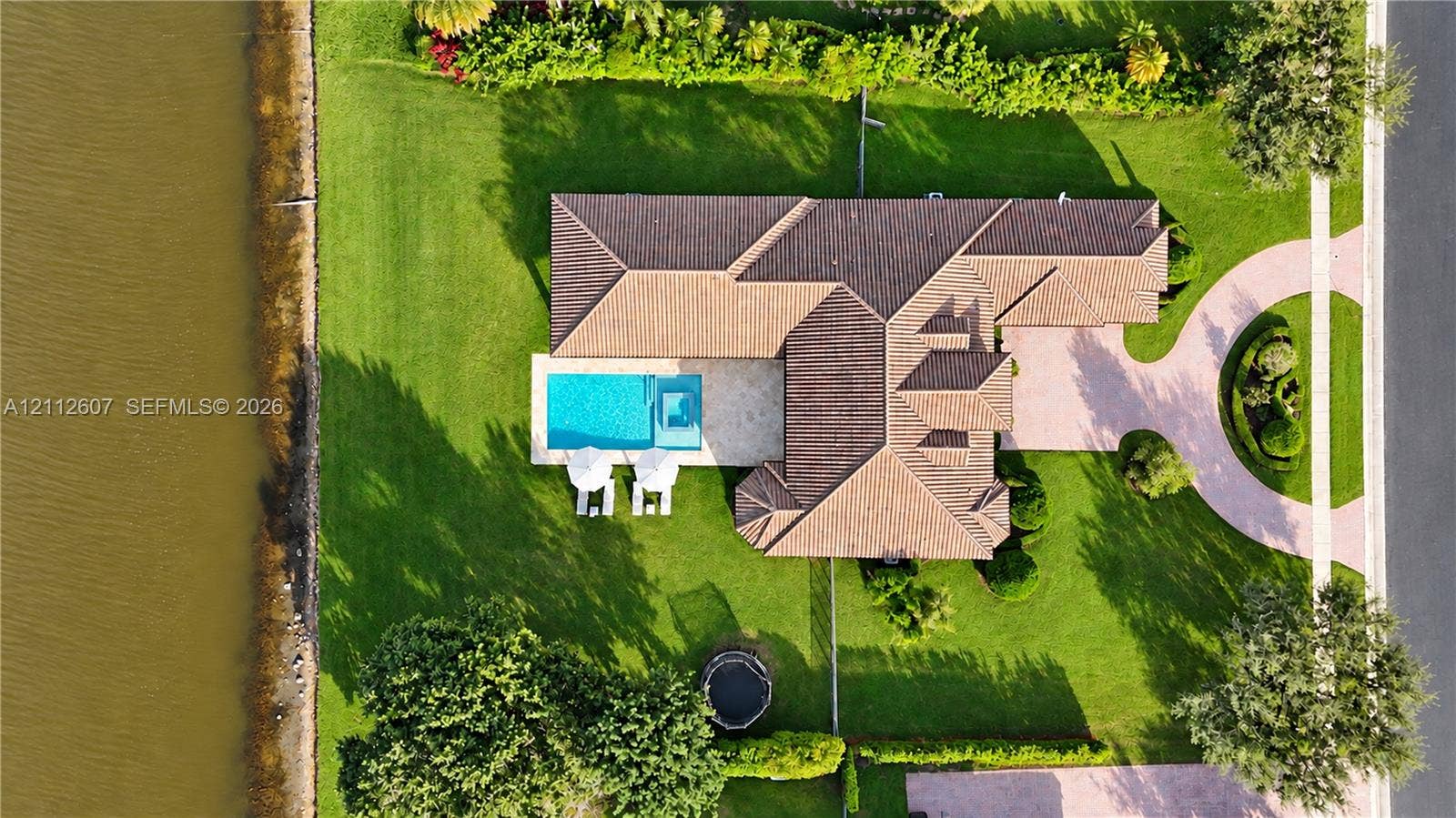 14443 S Jockey Circle S, Davie, FL 33330 Aerial perspective of a waterfront property featuring a tile roof, an in-ground swimming pool with an integrated spa, and paved circular driveway