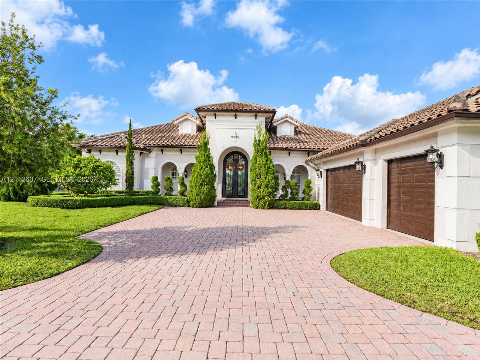 14443 S Jockey Circle S, Davie, FL 33330 Mediterranean-style exterior featuring a paved stone driveway, arched entryways, tile roof, and multi-car garage with wood-finish doors