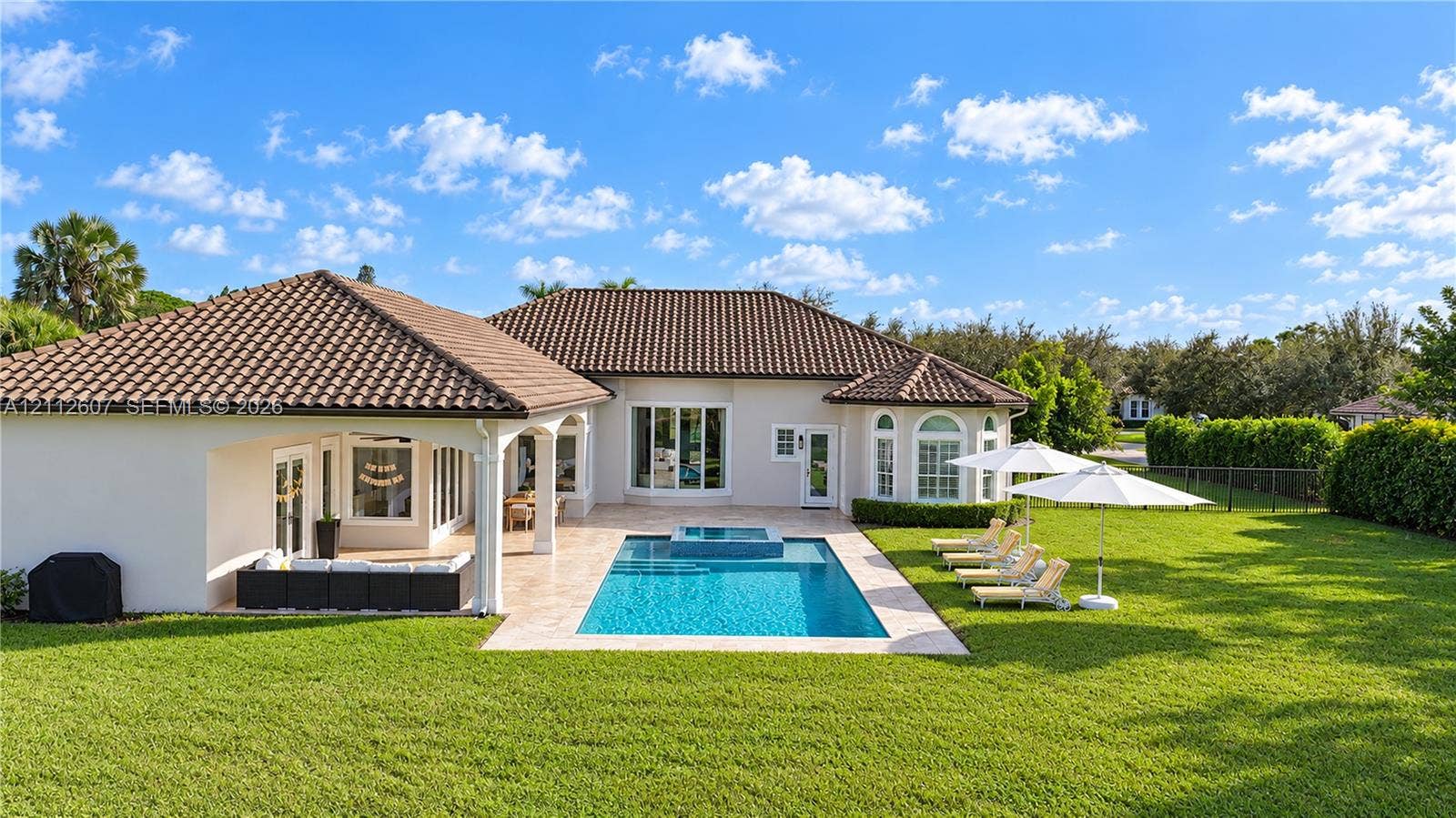 14443 S Jockey Circle S, Davie, FL 33330 Exterior featuring a tiled roof, covered patio, swimming pool with integrated spa, paved pool deck, and expansive lawn