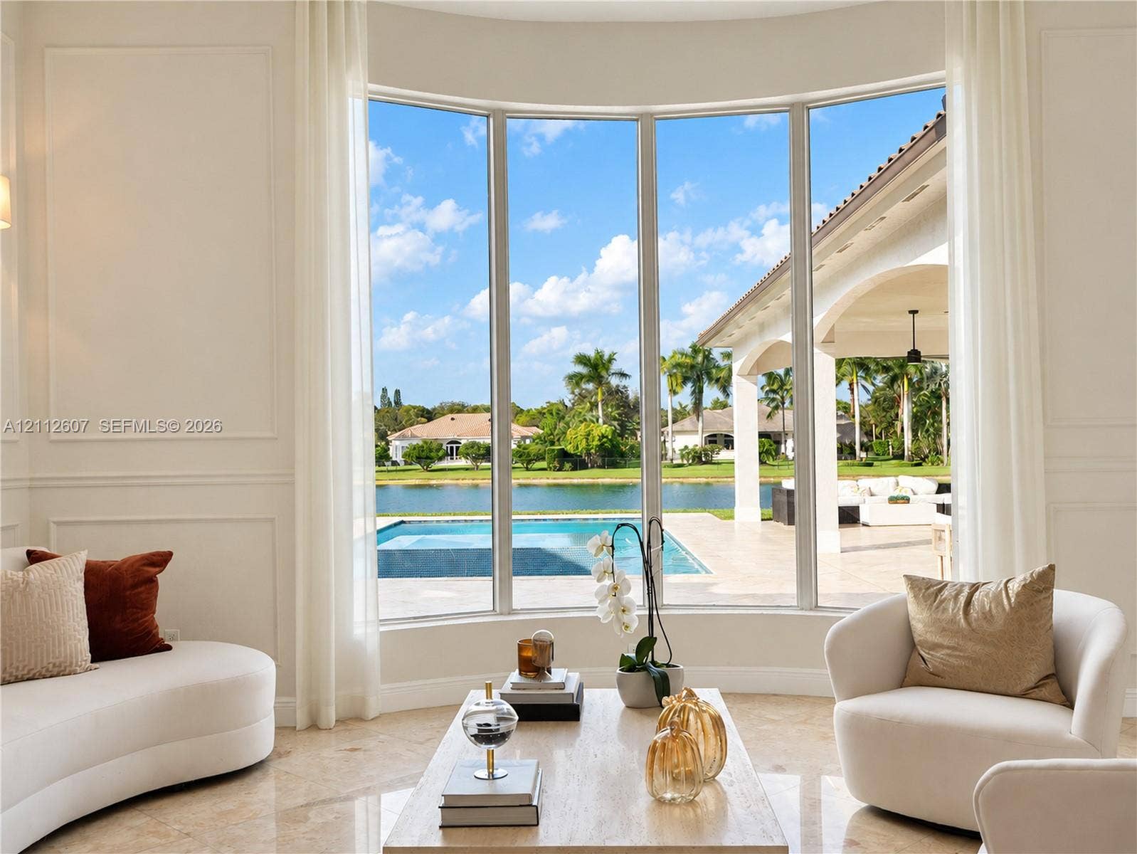 14443 S Jockey Circle S, Davie, FL 33330 Curved floor-to-ceiling windows, wall paneling, and polished stone flooring, featuring exterior access to a covered lanai, private pool, and water frontage