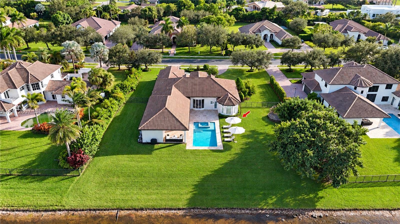 14443 S Jockey Circle S, Davie, FL 33330 Expansive waterfront lot featuring a rectangular swimming pool, integrated spa, covered patio, and manicured lawn