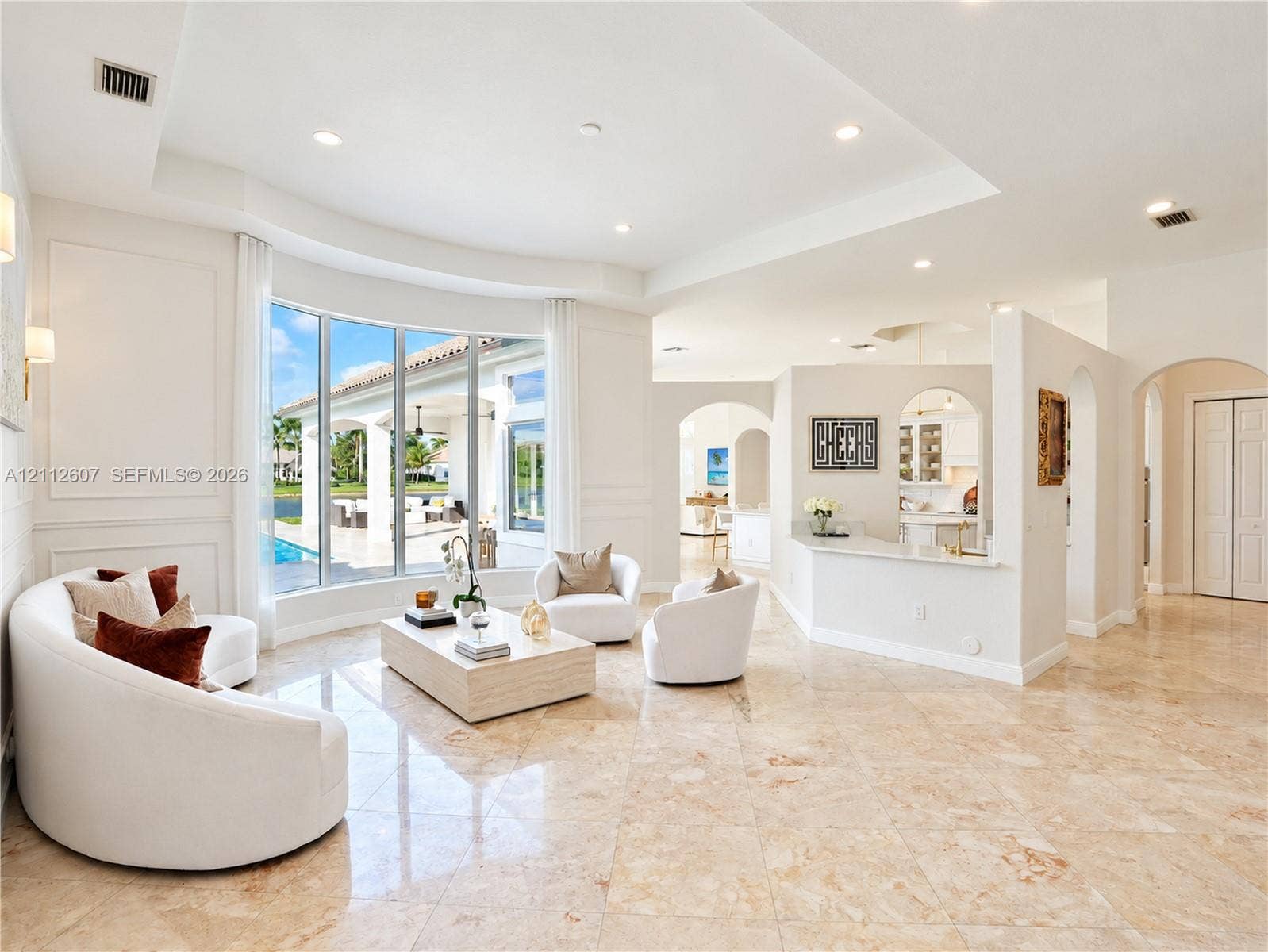 14443 S Jockey Circle S, Davie, FL 33330 Spacious living area featuring polished stone flooring, a tray ceiling, curved bay windows, and a built-in partition wall with an integrated breakfast bar