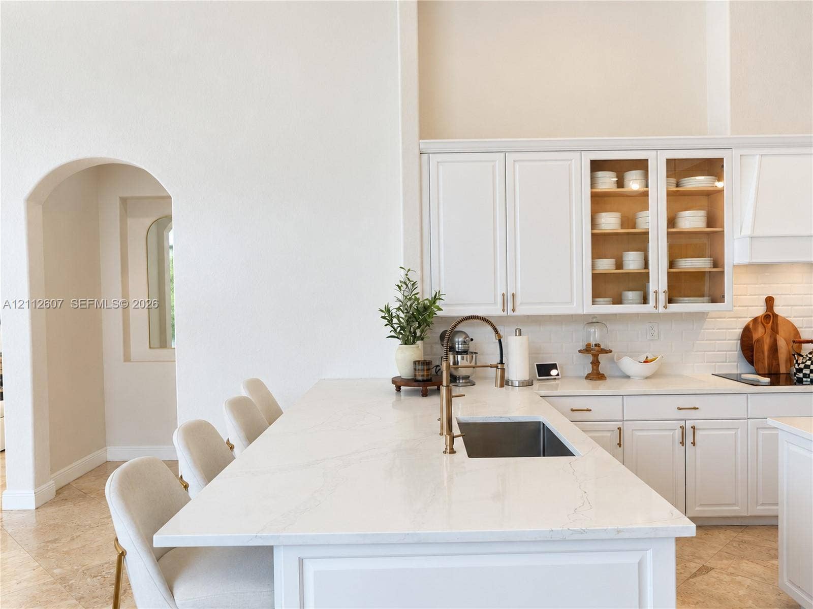 14443 S Jockey Circle S, Davie, FL 33330 Kitchen featuring white cabinetry, an expansive island with stone-finish countertops, subway tile backsplash, and an arched entry