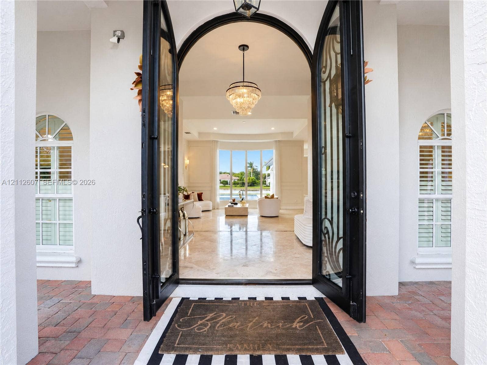 14443 S Jockey Circle S, Davie, FL 33330 Arched double entry doors with decorative iron detailing, flanked by arched windows with plantation shutters, polished stone flooring, and a multi-tiered crystal pendant light fixture