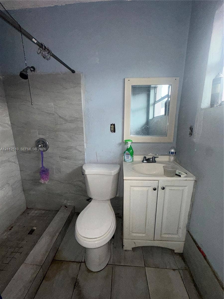 Hialeah, FL 33013 Bathroom featuring a tiled shower enclosure, a white vanity with an integrated sink, a wall-mounted mirror, and tile flooring