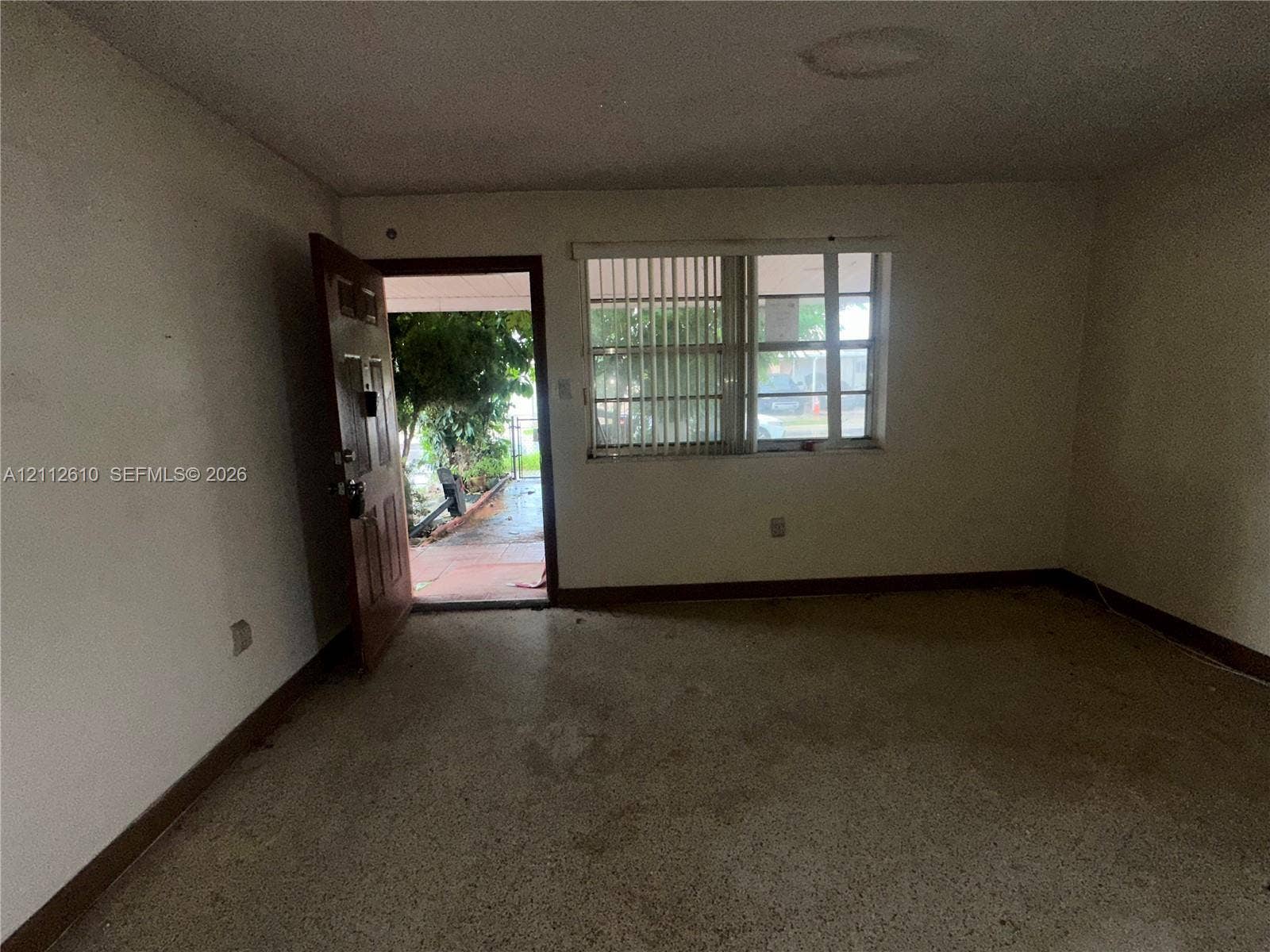 Hialeah, FL 33013 Interior space featuring a horizontal sliding window with vertical blinds, a solid wood-paneled entrance door, and neutral-toned flooring