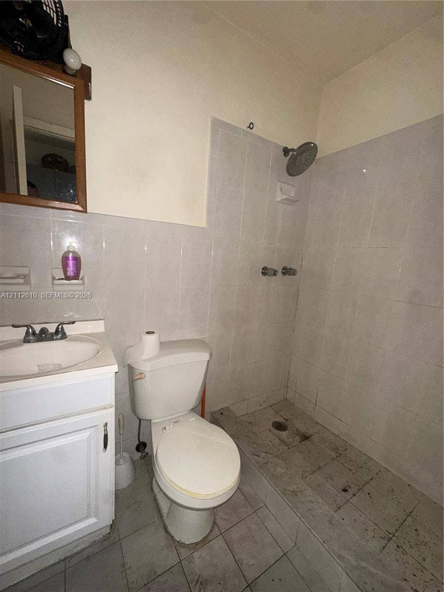 Hialeah, FL 33013 Bathroom featuring a white vanity cabinet, ceramic sink with chrome hardware, standard toilet, and a tiled shower stall with wall-mounted showerhead