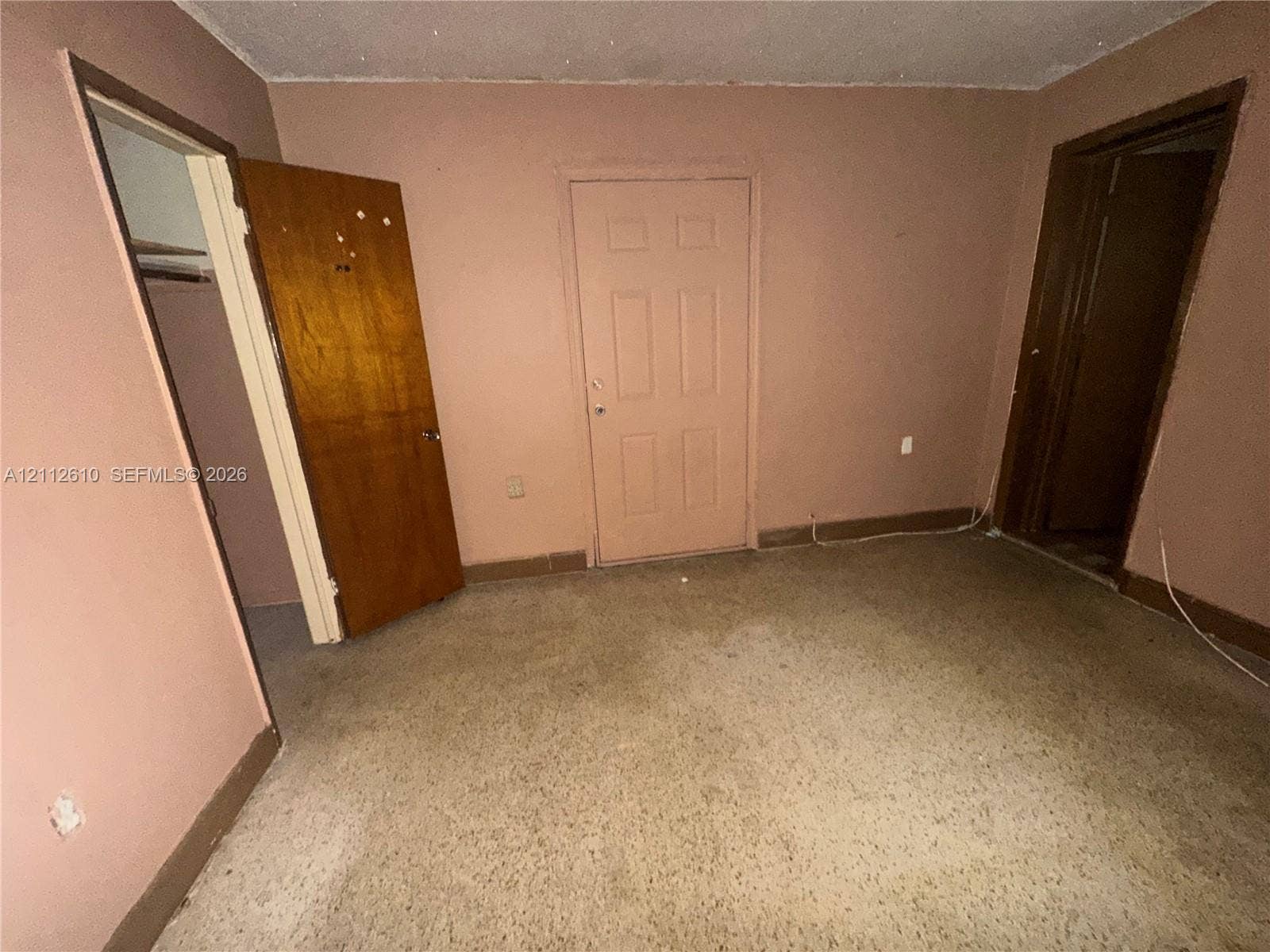 Hialeah, FL 33013 Interior room featuring neutral-toned wall paint, carpeted flooring, a six-panel door, and two entryways leading to separate spaces