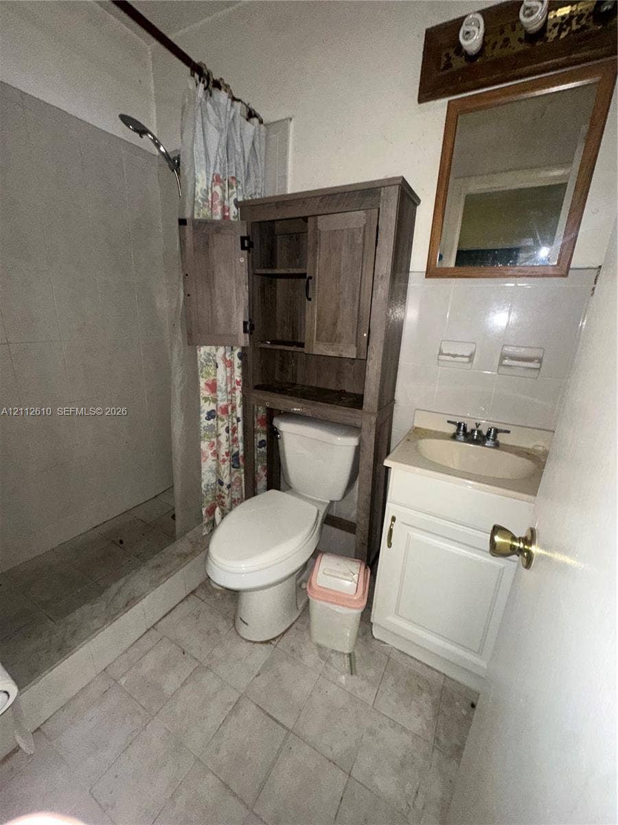 Hialeah, FL 33013 Bathroom featuring a walk-in shower with tiled surround, a vanity with a drop-in sink, a wall-mounted mirror, and tile flooring