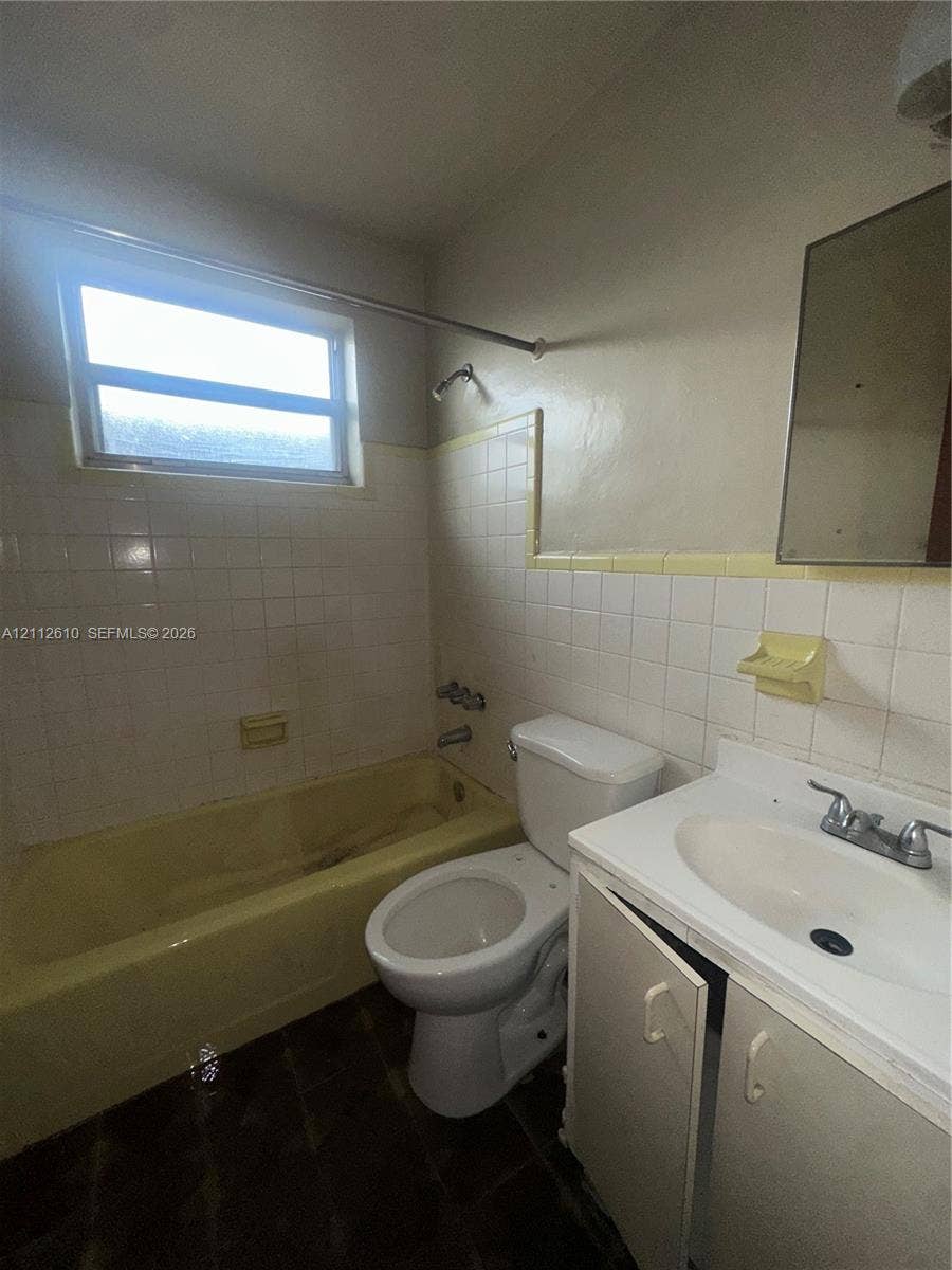 Hialeah, FL 33013 Bathroom featuring a built-in bathtub, a wall-mounted medicine cabinet, white tiled wall surrounds, and a vanity cabinet with an integrated sink