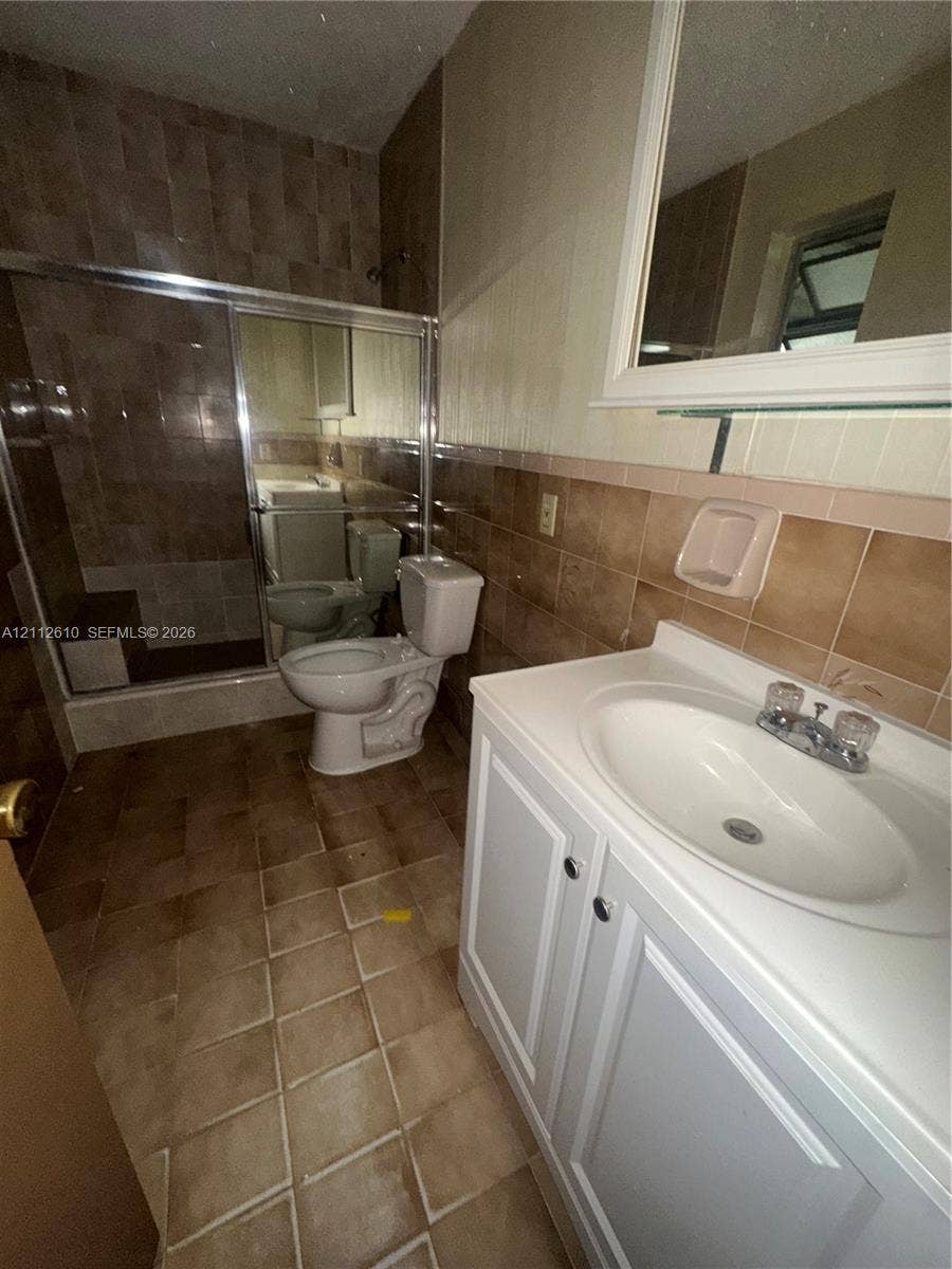 Hialeah, FL 33013 Bathroom featuring a white vanity cabinet with an integrated sink, shower enclosure with tiled walls, ceramic floor tiling, and a wall-mounted mirror