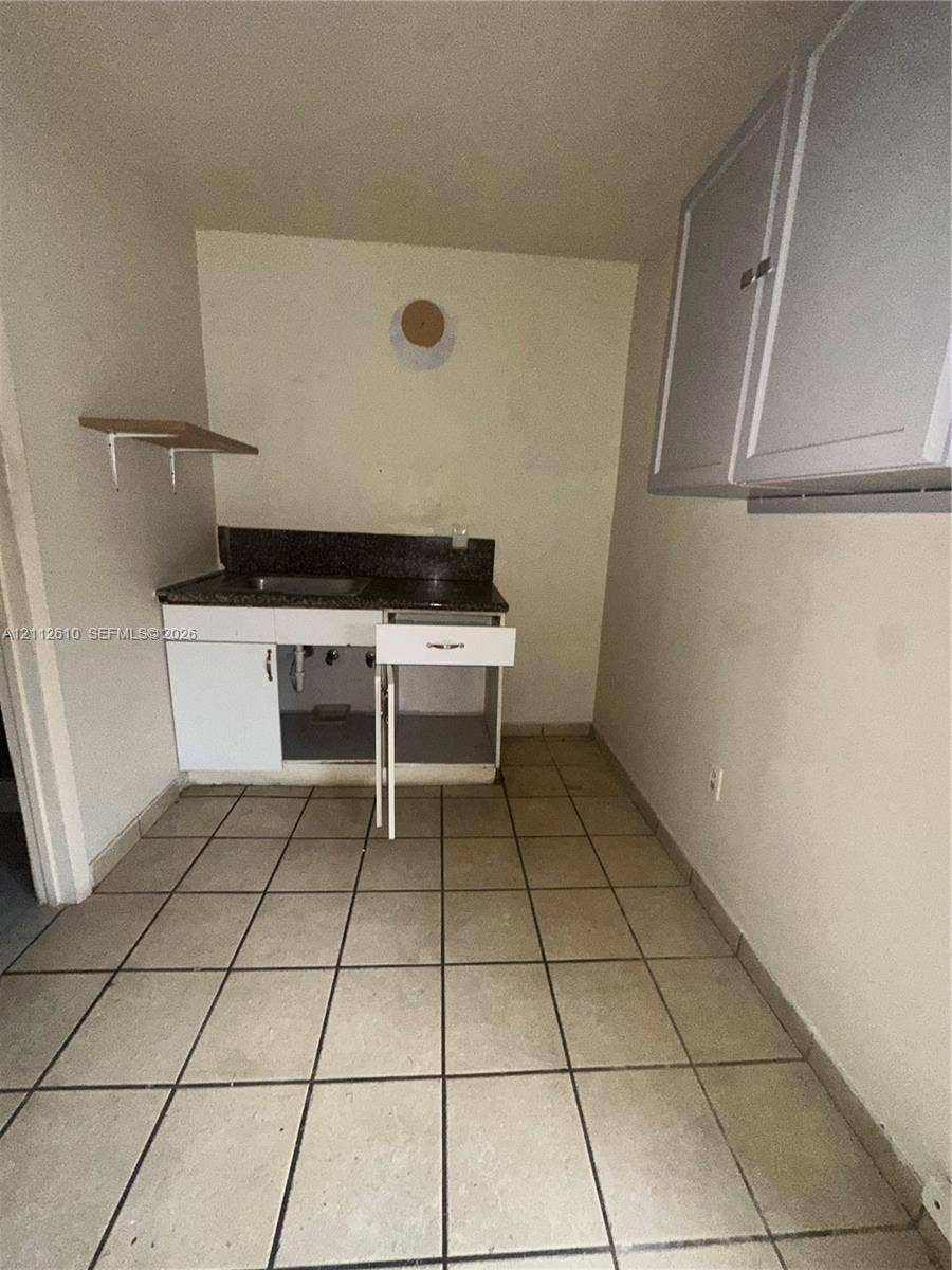 Hialeah, FL 33013 Kitchenette featuring a stone-finish countertop, stainless steel sink, lower cabinetry with integrated drawer, wall-mounted upper cabinetry, and ceramic tile flooring
