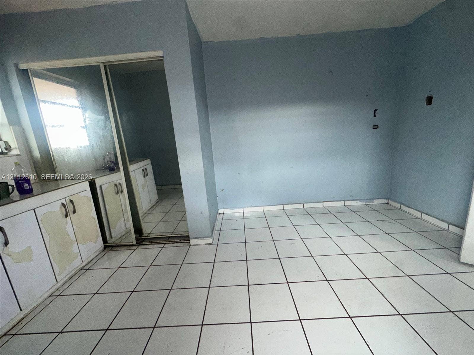 Hialeah, FL 33013 Room interior featuring white tile flooring, built-in cabinetry with hardware, and sliding mirrored closet doors