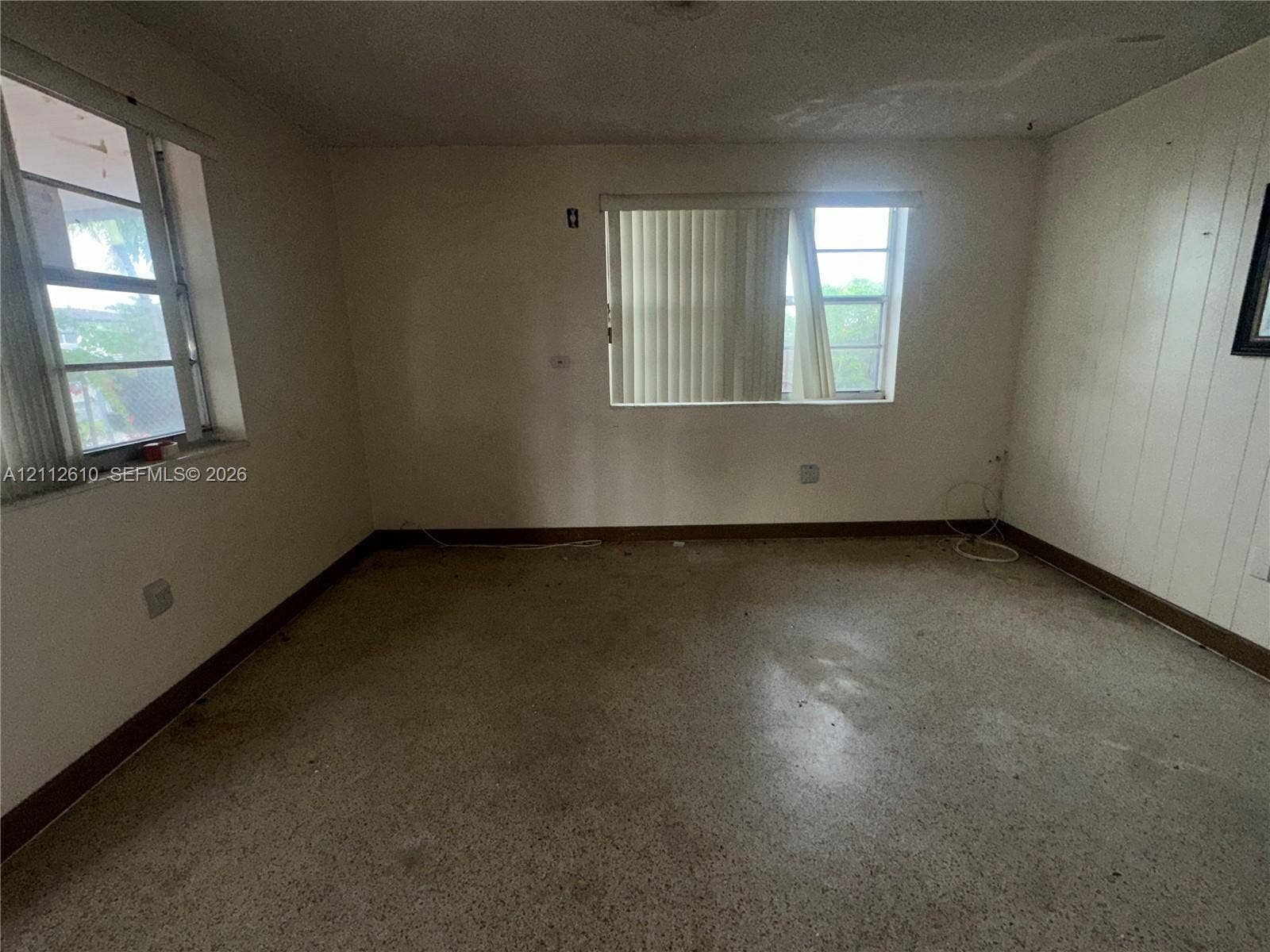Hialeah, FL 33013 Interior space featuring terrazzo flooring, paneling on one wall, and two windows with horizontal blinds