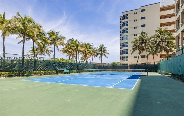 Hard-surface tennis court featuring perimeter privacy fencing and palm tree landscaping