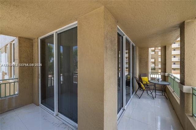 Covered balcony featuring white tiled flooring, stucco walls, dual sliding glass door access, and green metal railings