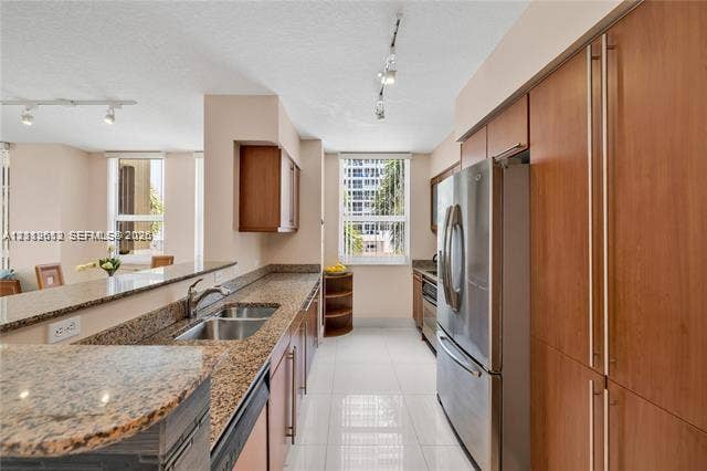 Kitchen featuring wood-veneer cabinetry, stone countertops, stainless steel appliances, dual-basin under-mount sink, and large-format tile flooring