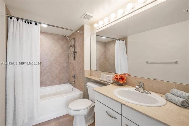 Bathroom featuring a recessed tub with a tile surround, a built-in vanity with a solid-surface countertop, an integrated oval sink, and a full-width wall mirror with an integrated light fixture