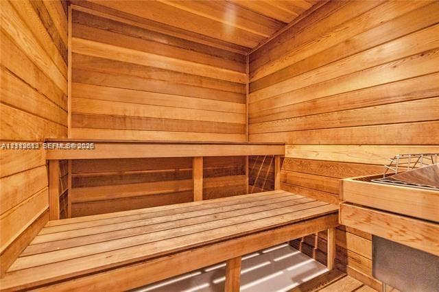 Sauna featuring natural wood tongue-and-groove paneling, tiered wood bench seating, and a built-in heating element