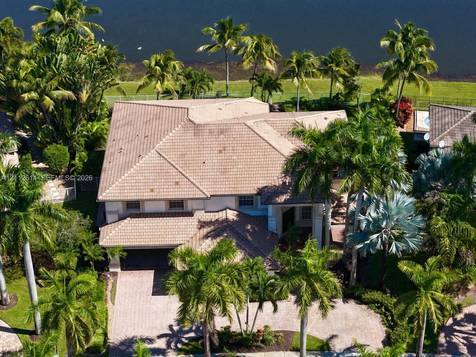 1422 Victoria Isle Drive, Weston, FL 33327 Multi-level residence featuring a tile roof, paved driveway, and mature landscaping on a waterfront lot