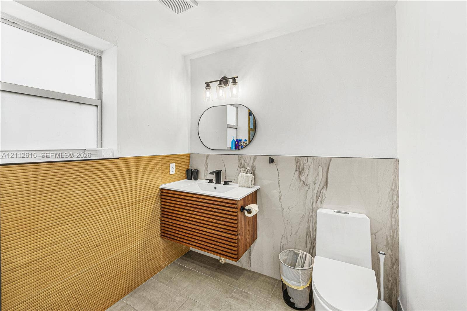 817 Tyler Street, #9, Hollywood, Hollywood, FL 33019 Wall-mounted vanity featuring slatted wood cabinetry, rectangular sink, and matte black faucet, accented by textured wood-finish wall panels, large-format stone-patterned tile wall cladding, and an oval mirror with three-light fixture