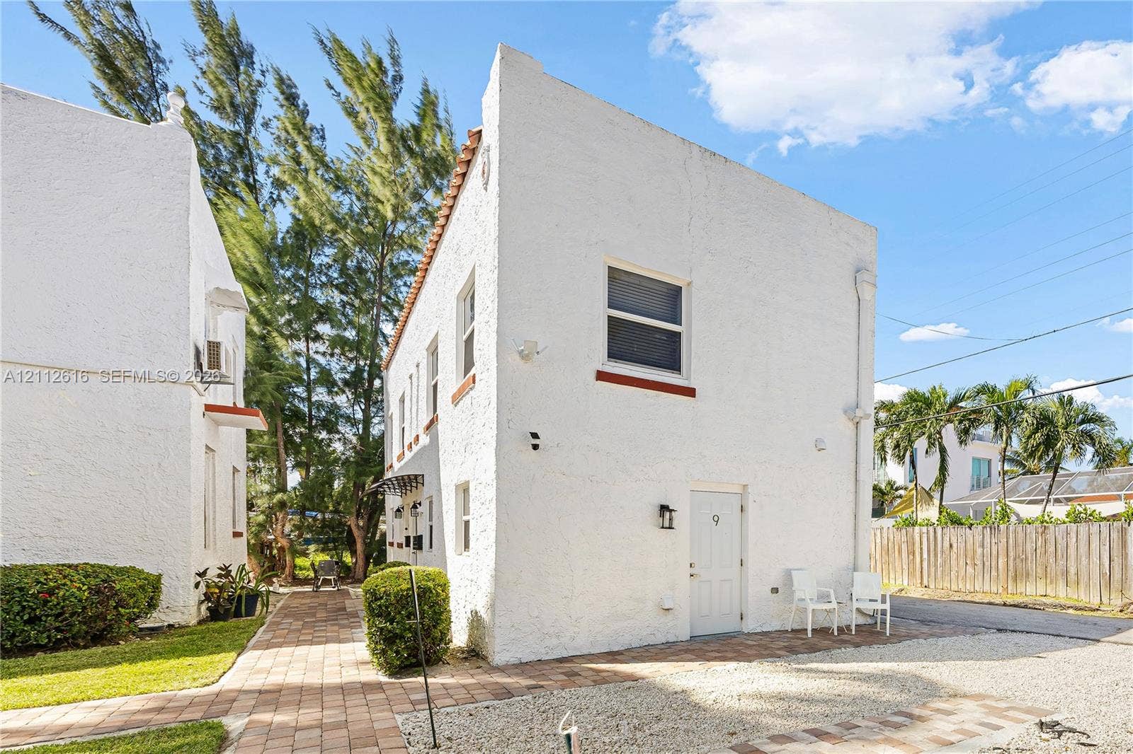 817 Tyler Street, #9, Hollywood, Hollywood, FL 33019 Two-story structure featuring a white textured exterior, terracotta roof detailing, a paved walkway, and an attached exterior light fixture