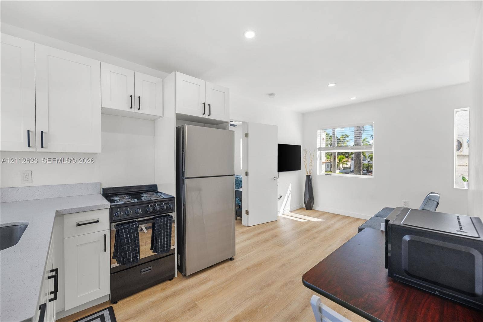 817 Tyler Street, #10, Hollywood, Hollywood, FL 33019 Kitchen featuring white shaker-style cabinetry, stainless steel appliances, light-toned solid surface countertops, and wood-finish flooring