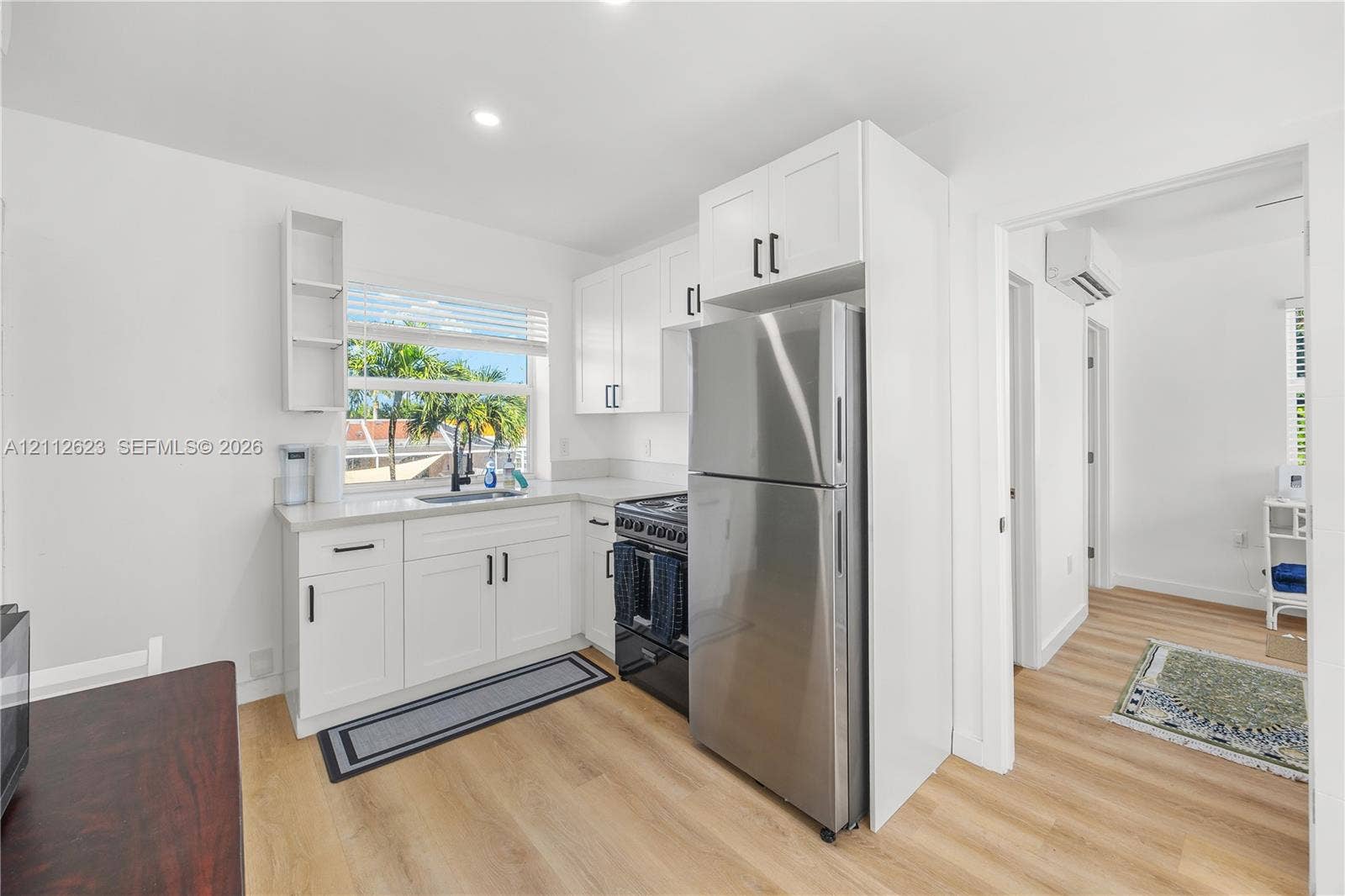 817 Tyler Street, #10, Hollywood, Hollywood, FL 33019 Kitchen featuring white cabinetry with black hardware, stainless steel refrigerator, dark range, light-toned wood-finish flooring, and quartz countertops