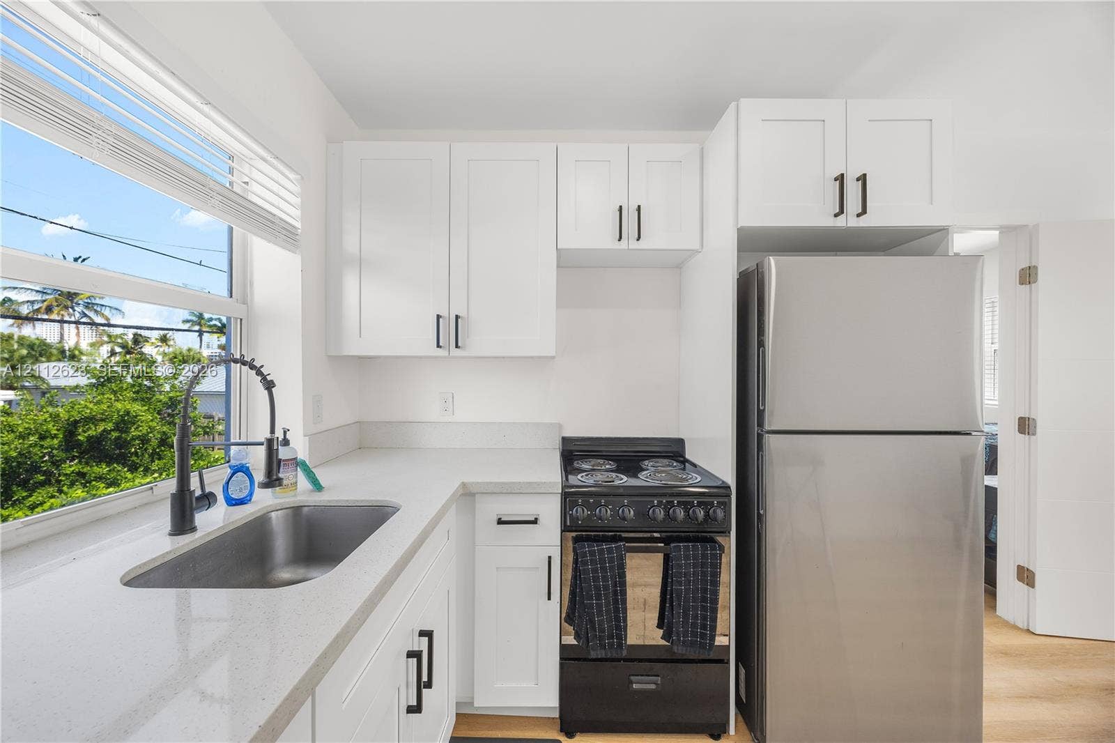 817 Tyler Street, #10, Hollywood, Hollywood, FL 33019 Kitchen featuring white shaker-style cabinetry, matte black hardware, stone-finish countertops, stainless steel refrigerator, and high-arc pull-down faucet