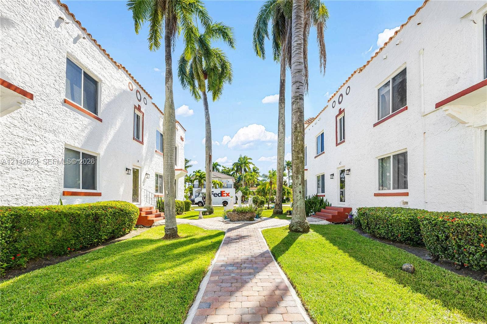 817 Tyler Street, #10, Hollywood, Hollywood, FL 33019 Stucco exterior featuring dual buildings with terracotta roof accents, manicured lawns, mature palm trees, and a central brick-paver walkway