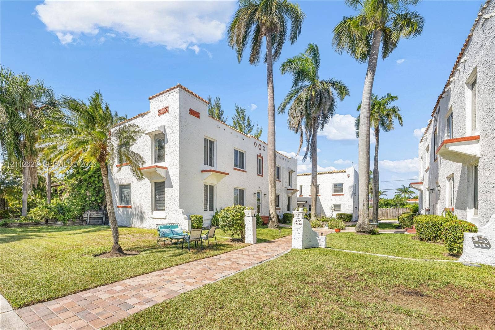817 Tyler Street, #10, Hollywood, Hollywood, FL 33019 Mediterranean-style architecture featuring textured white stucco exterior, clay-tile roof accents, decorative architectural molding, paver walkway, and mature palm trees