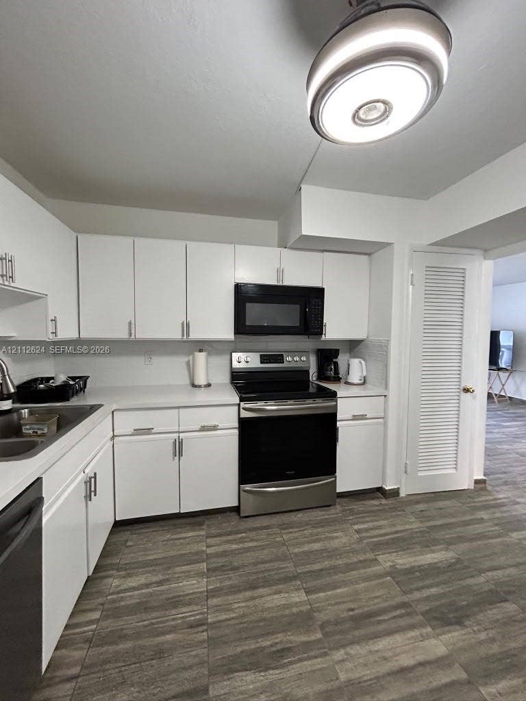 Kitchen featuring white cabinetry with brushed nickel hardware, stainless steel appliances, a modern flush-mount light fixture, and wood-finish tile flooring