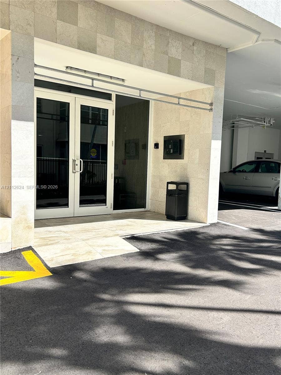 Building entrance featuring dual-panel glass doors, natural stone tile facade, and integrated electronic security access system