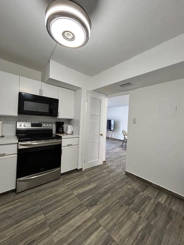 Kitchen featuring white cabinetry, stainless steel oven and microwave, wood-finish flooring, and circular flush-mount ceiling lighting