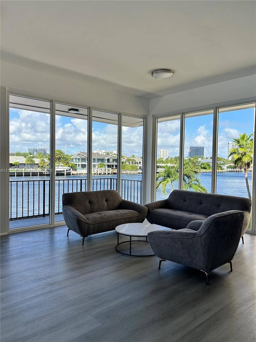 Floor-to-ceiling windows featuring panoramic water scenery, wood-finish flooring, and a metal-railed balcony