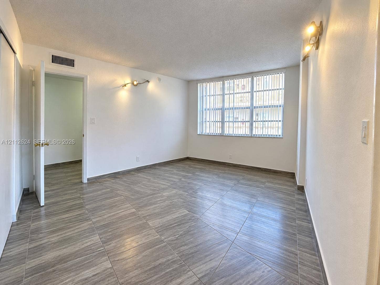 Interior room featuring large-format wood-finish tile flooring, vertical blinds over a multi-pane window, and wall-mounted light fixtures