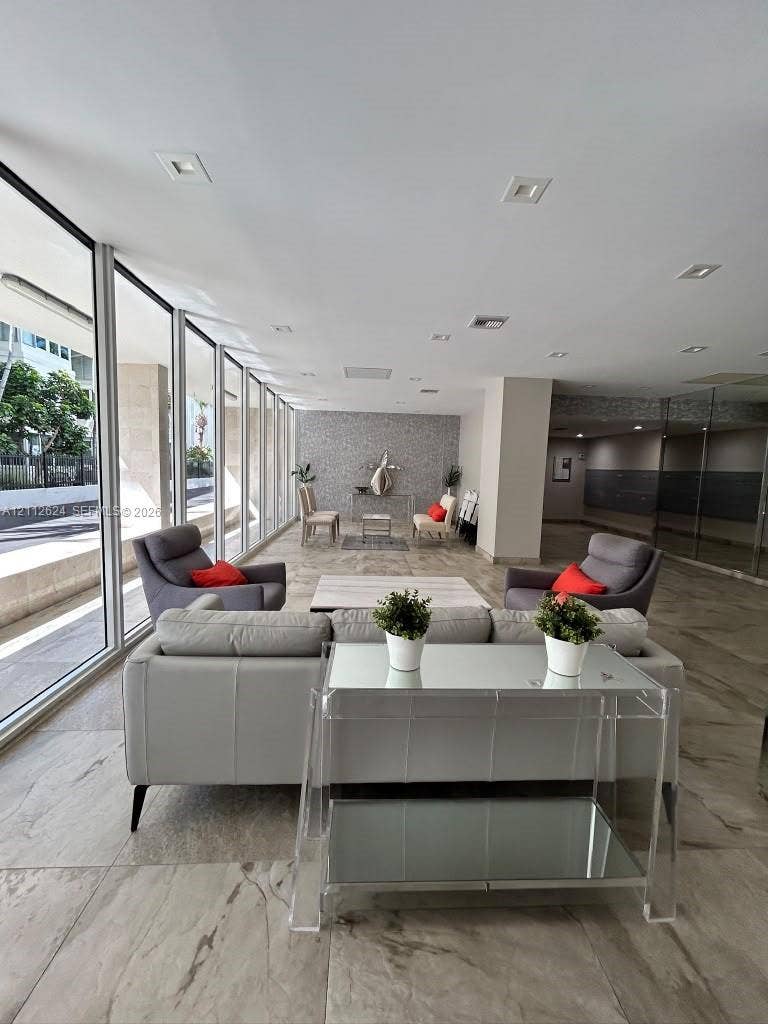 Floor-to-ceiling glass windows, recessed ceiling lighting, large-format tiled flooring, and a textured stone-finish accent wall