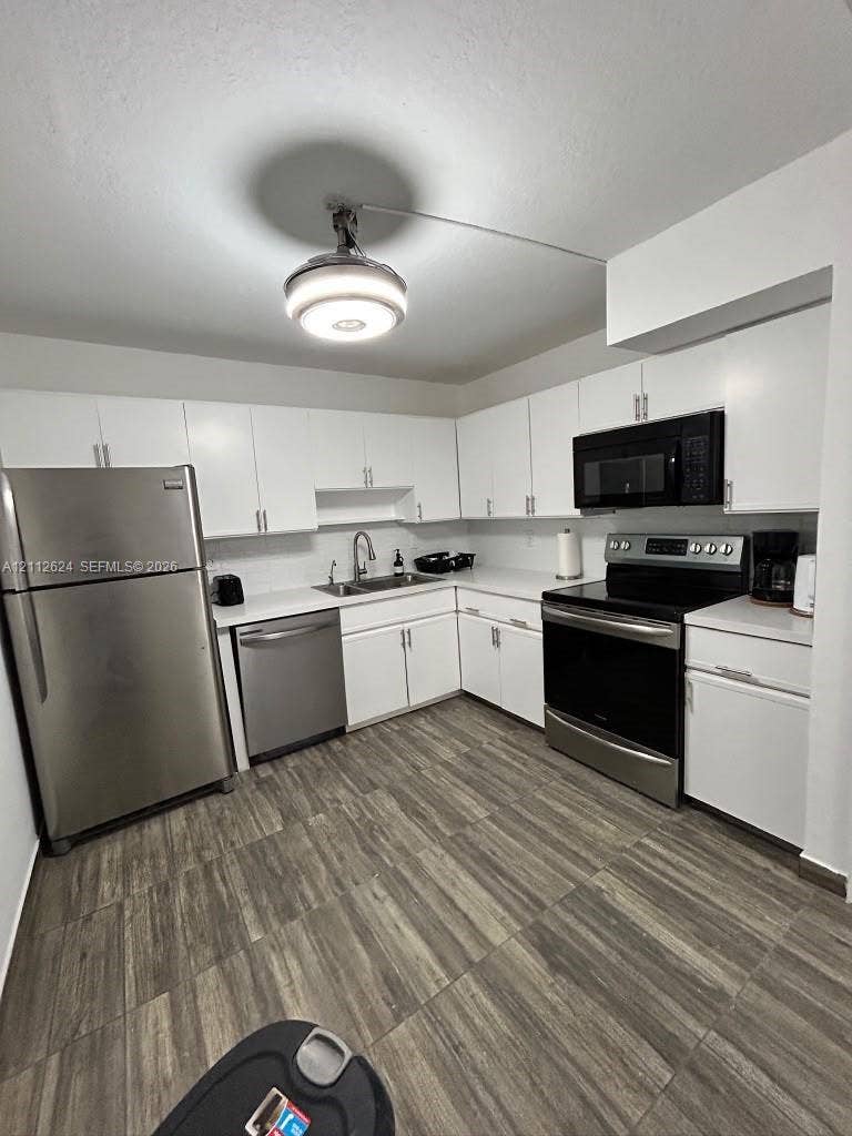 Kitchen featuring white cabinetry, solid-surface countertops, stainless steel appliances, and wood-finish flooring