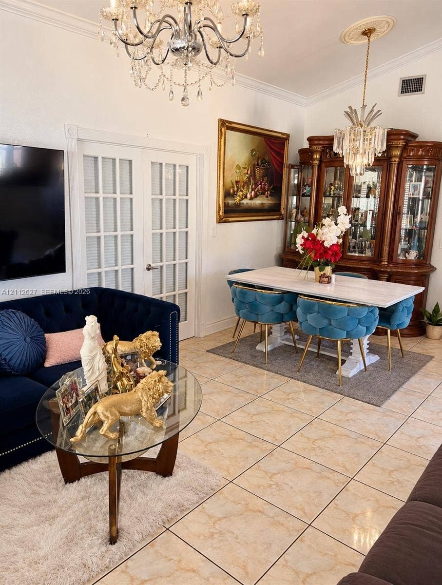 240 E 39th Street, Hialeah, FL 33013 Interior space featuring large-format tile flooring, crown molding, double French doors, and decorative crystal chandeliers with ceiling medallions