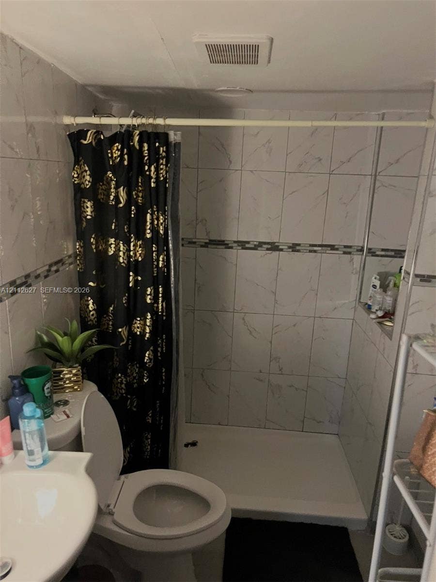 240 E 39th Street, Hialeah, FL 33013 Bathroom featuring a walk-in shower with white veined tile surround, decorative mosaic tile accents, and a built-in recessed shelf