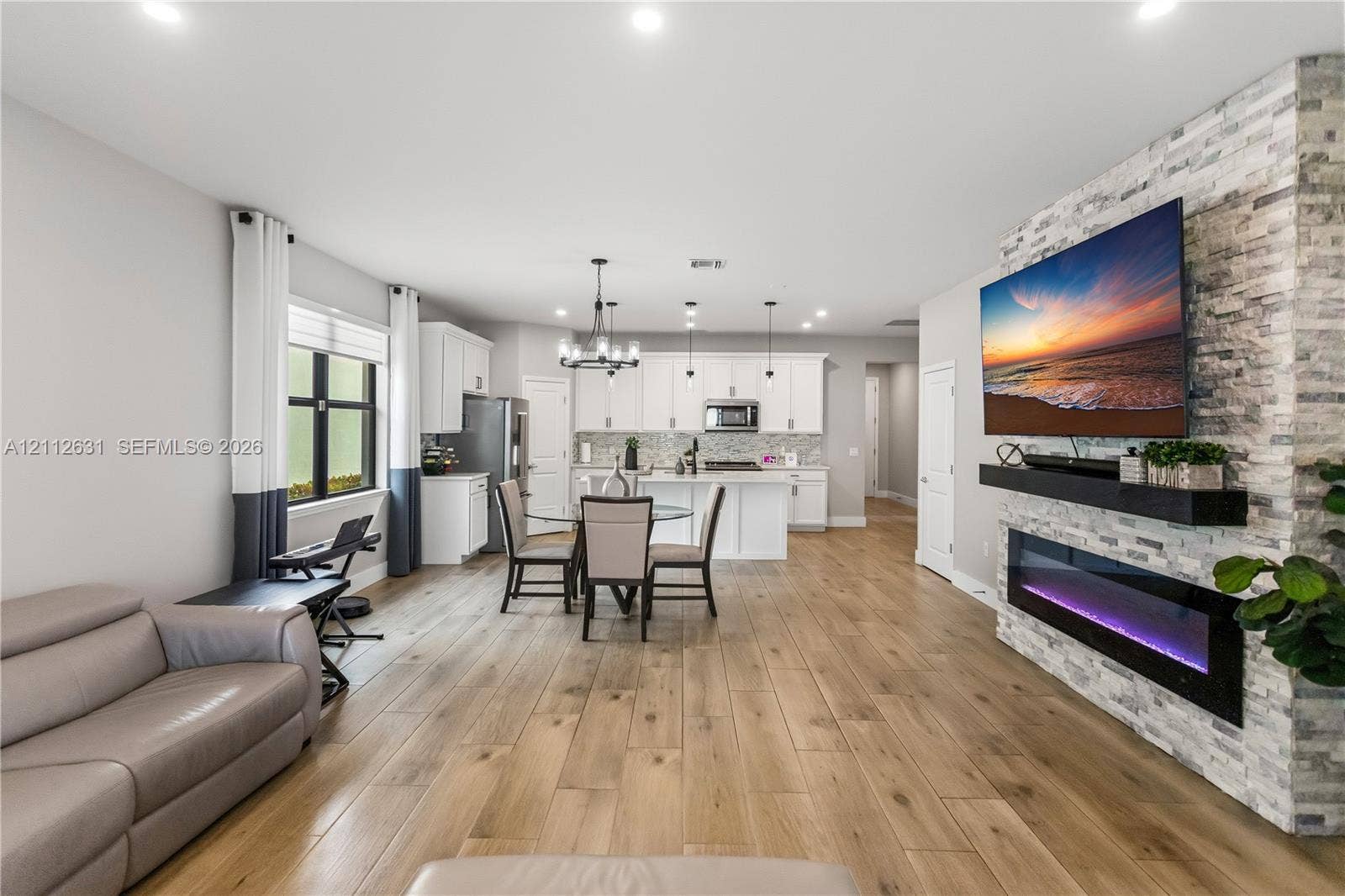 8257 NW 79th Avenue, Tamarac, FL 33321 Open-concept interior featuring wood-finish flooring, a full-height stone-clad fireplace with an integrated linear electric insert, white cabinetry, and recessed lighting