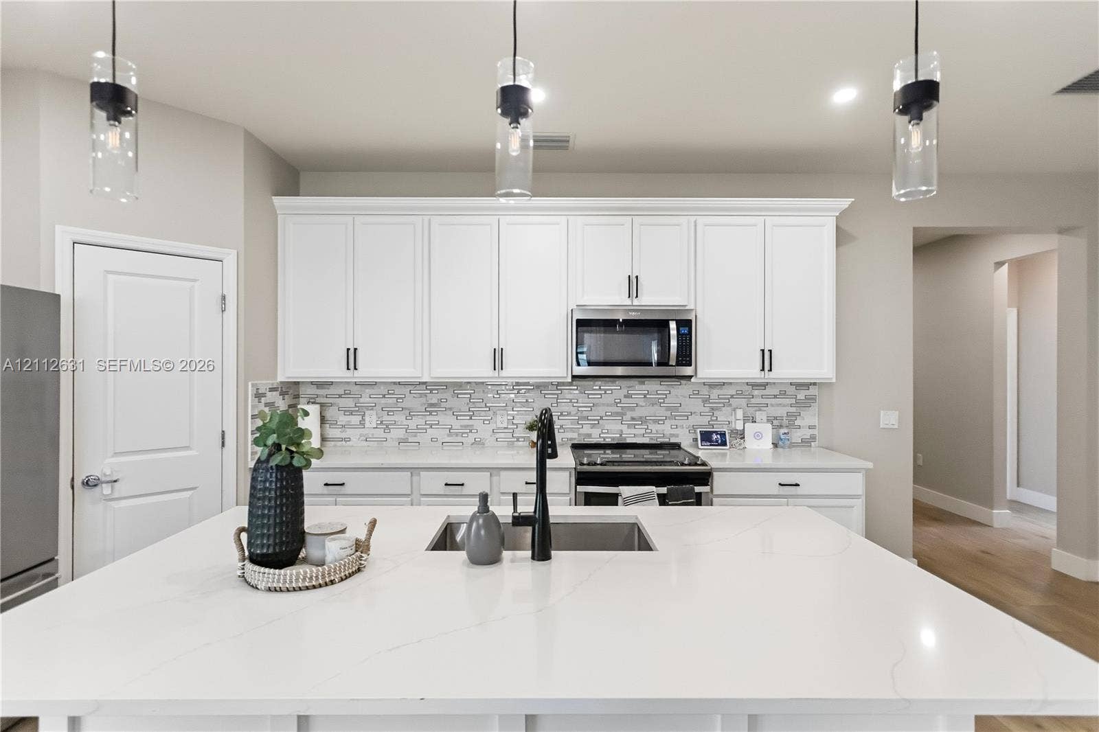 8257 NW 79th Avenue, Tamarac, FL 33321 Kitchen featuring an oversized island with a solid surface countertop, white shaker-style cabinetry, a stone-patterned tile backsplash, matte black plumbing fixtures, and three cylindrical pendant lights