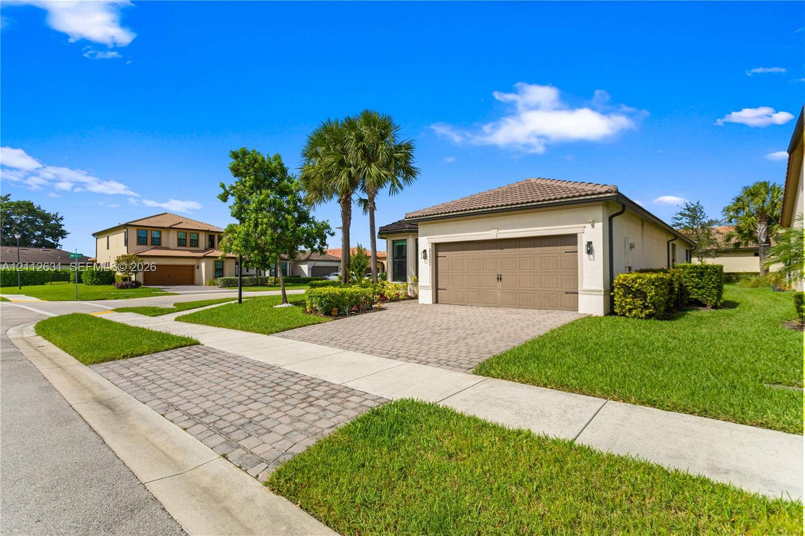 8257 NW 79th Avenue, Tamarac, FL 33321 Stucco exterior featuring a paver driveway, multi-car garage, and mature landscaping