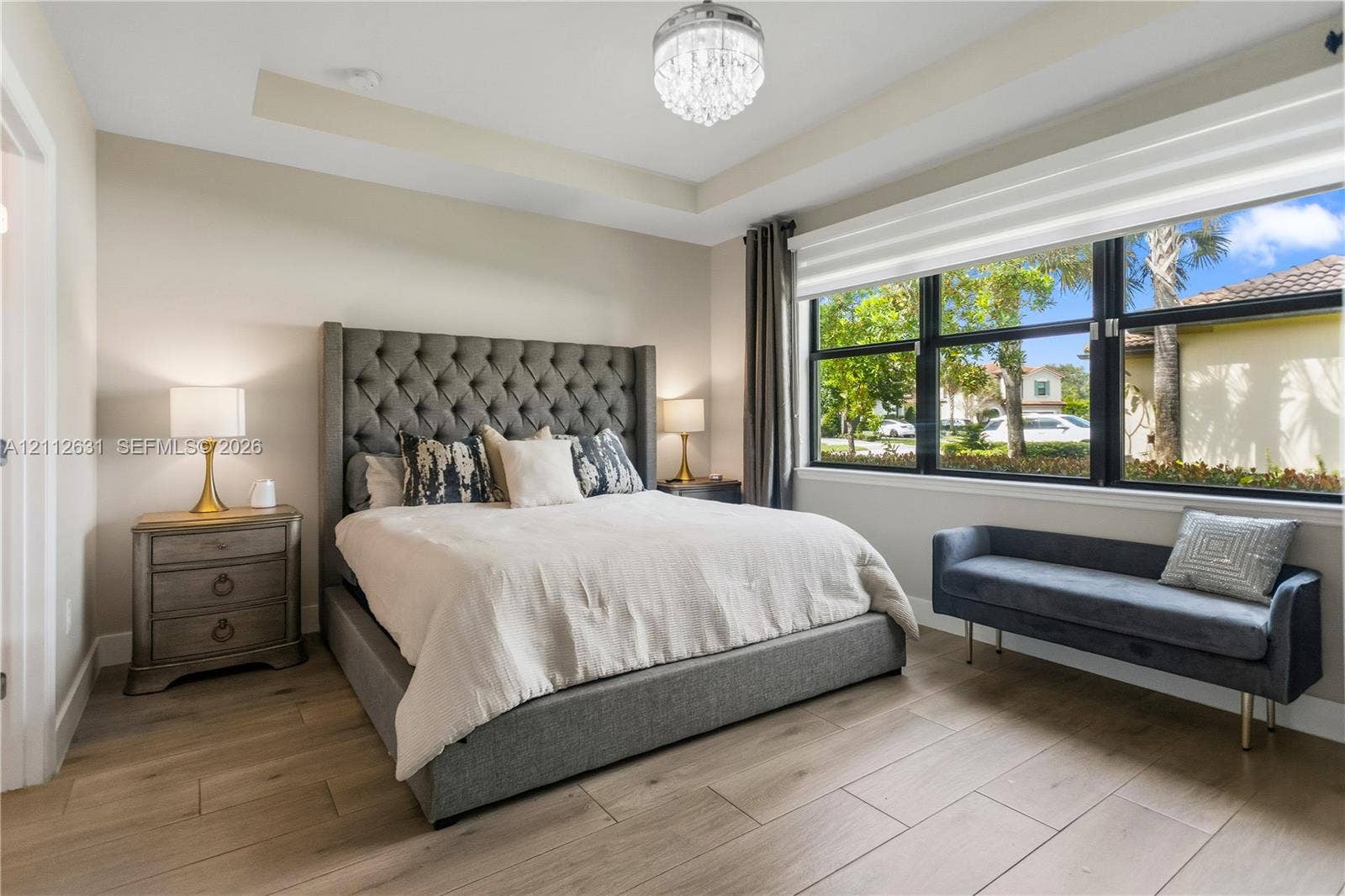 8257 NW 79th Avenue, Tamarac, FL 33321 Bedroom featuring wood-finish flooring, a tray ceiling, a multi-tiered crystal chandelier, and large windows with black frames